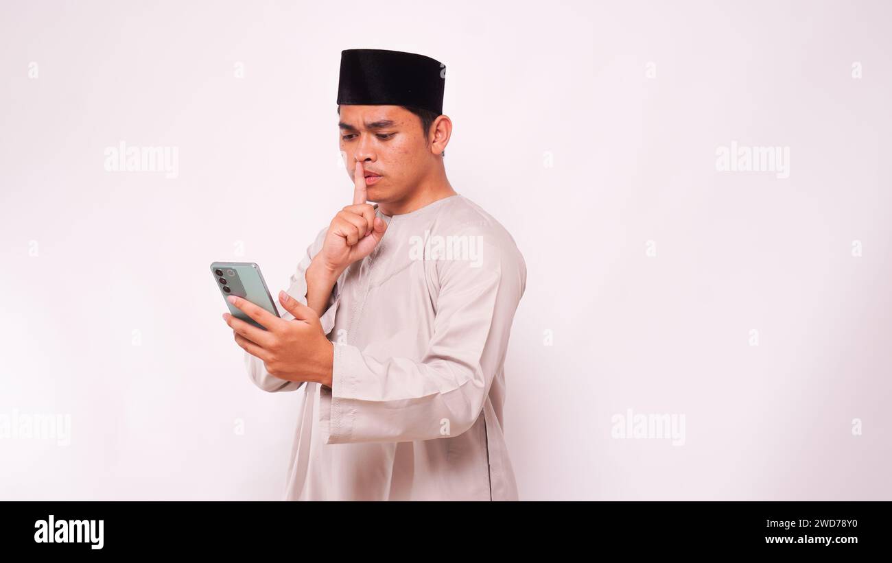 Asian muslim man holding smartphone and make a quite sign with his finger. isolated on white background Stock Photo