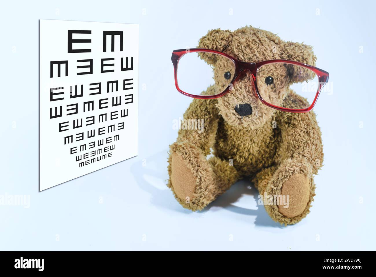 Little teddy bear with big red glasses sitting beside a pediatric vision screening chart, concept of eye care and ophthalmology for children, light bl Stock Photo
