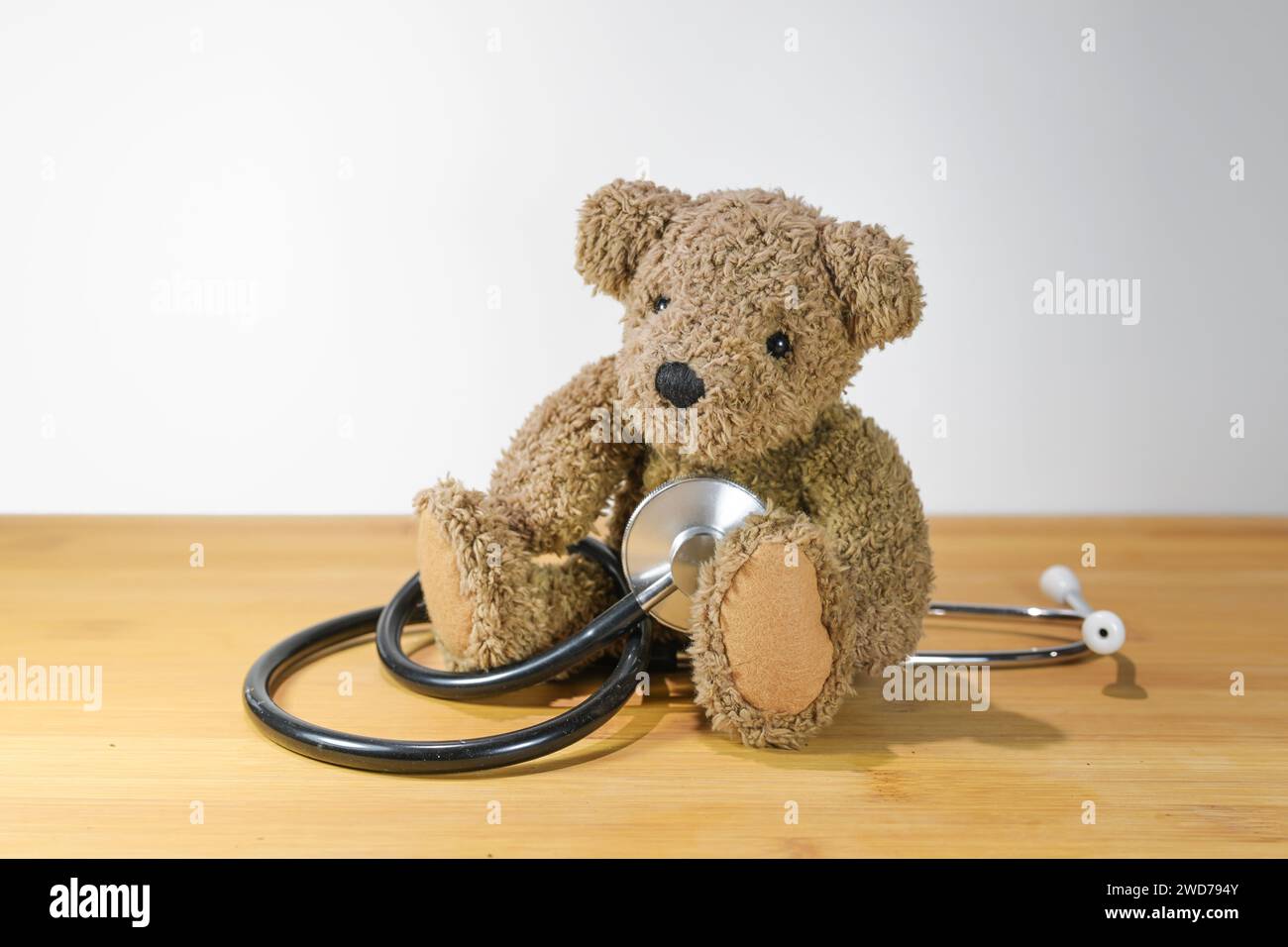 Little toddler teddy bear sitting on the table and playing with a stethoscope like a child, concept for pediatric medicine and health care, light gray Stock Photo