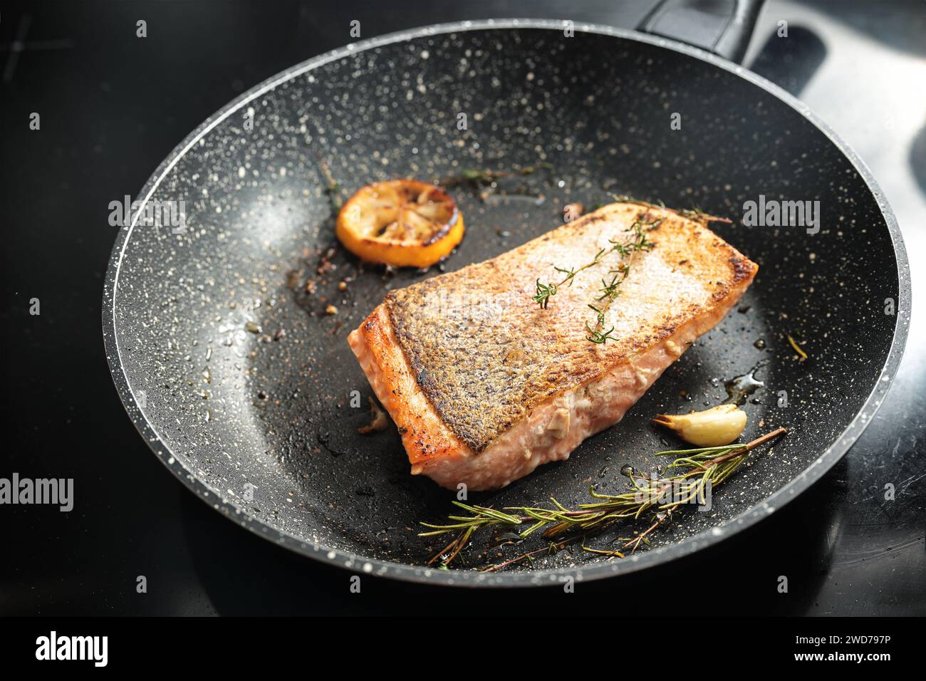 Rain trout fillet with a crispy fried skin, garlic, lemon and herbs in a frying pan, healthy cooking with fish, copy space, selected focus, narrow dep Stock Photo