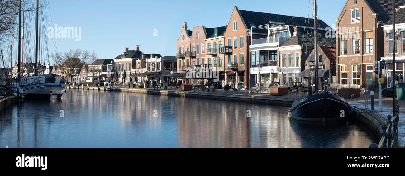 Panoramic view in winter of canal with Lemsteraak at the right, boats and houses mirrored in water in the center of Lemmer in Friesland, Netherlands Stock Photo