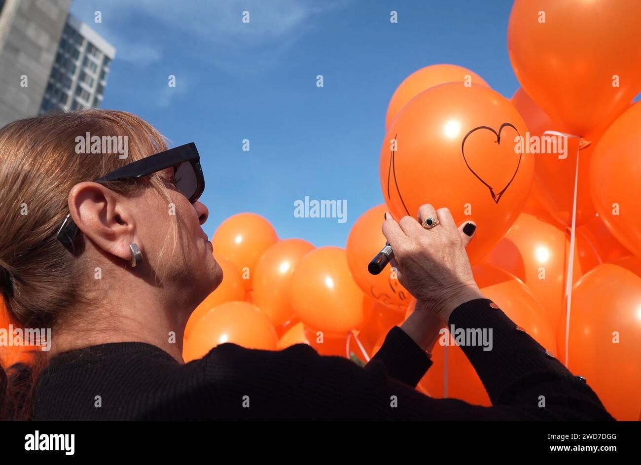 A woman writes on orange balloons during an event to mark the first birthday of Kfir Bibas, the youngest Israeli hostage taken into Gaza by Hamas militants at the plaza now called 'The Hostages and Missing Square' outside The Museum of Modern Art on January 18, 2024 in Tel Aviv, Israel. Stock Photo