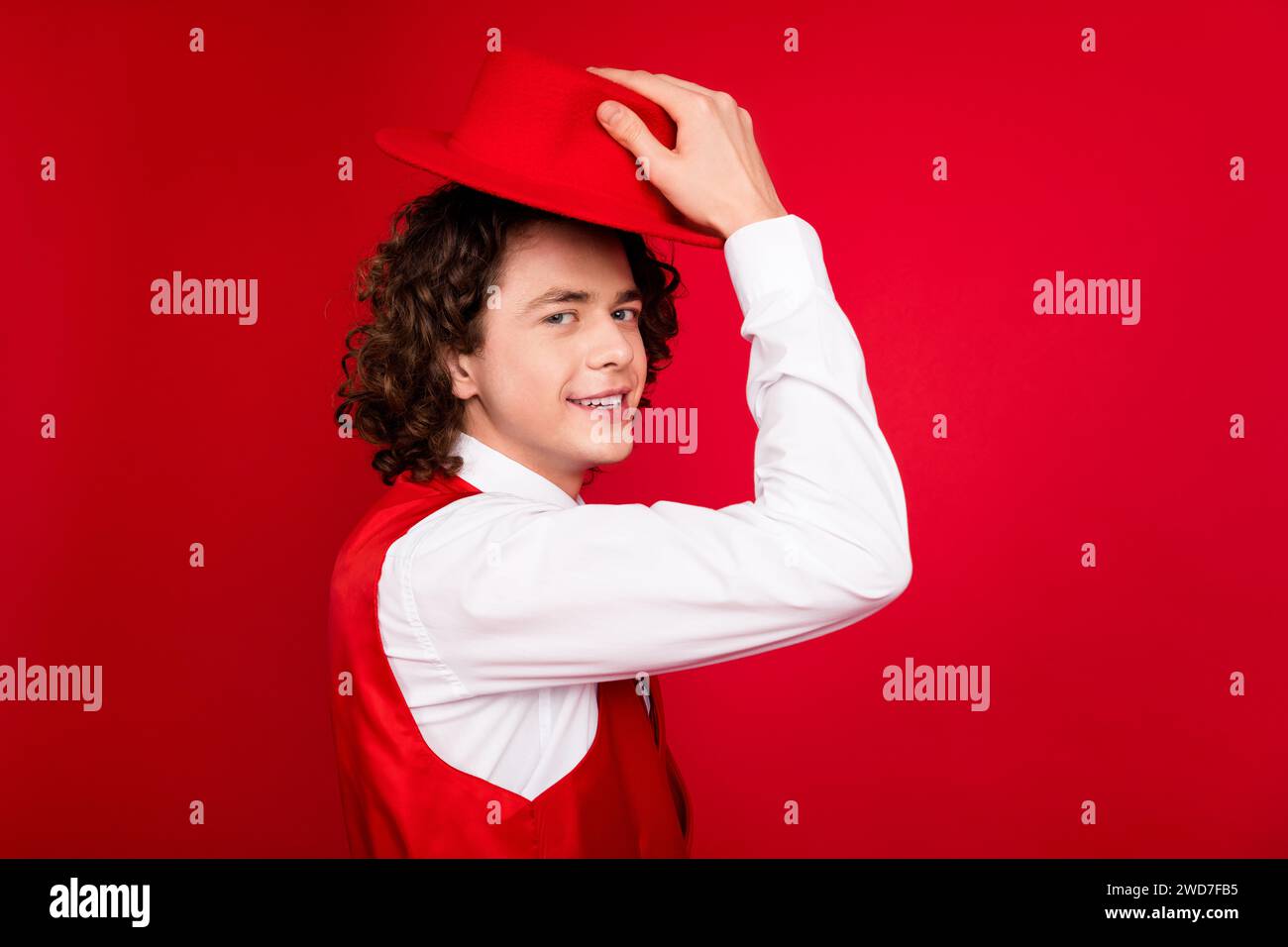 Closeup portrait of confident extravagant person teenager guy wearing shirt and vest touching hat isolated on red color background Stock Photo
