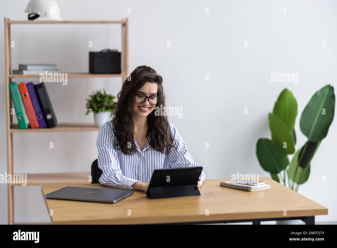 Attractive business woman using a digital tablet while standing in front of windows in an office Stock Photo