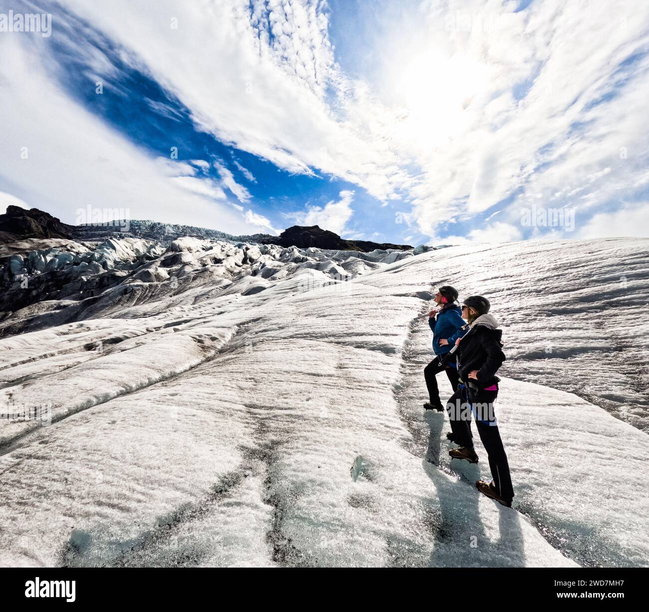 Sisters hike up glacier with spikes with sunshine and blue sky Stock Photo