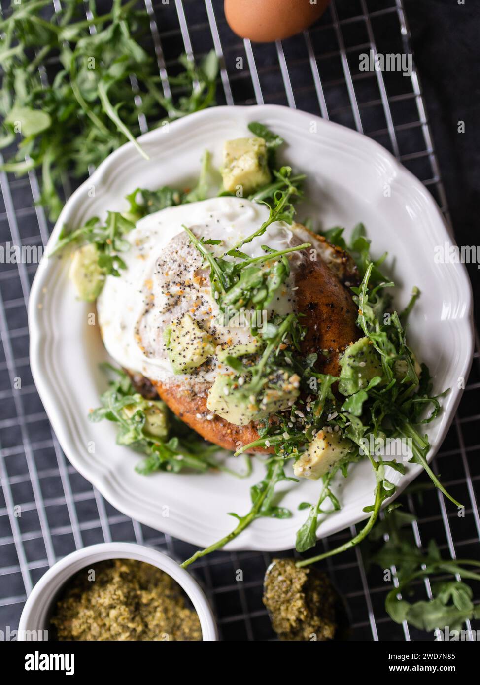 Savory egg and bagel breakfast topped with arugula, pesto, and avocado Stock Photo