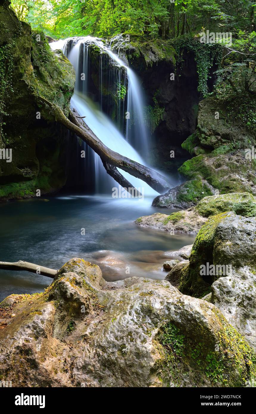 Waterfall cascading among lush vegetation and rocky terrain Stock Photo