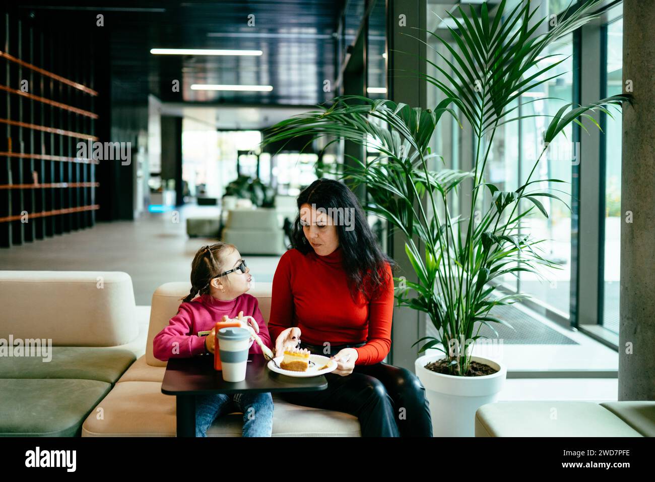 Portrait of loving mother and cute girl with down syndrome eating cake in cafe inside. Stock Photo