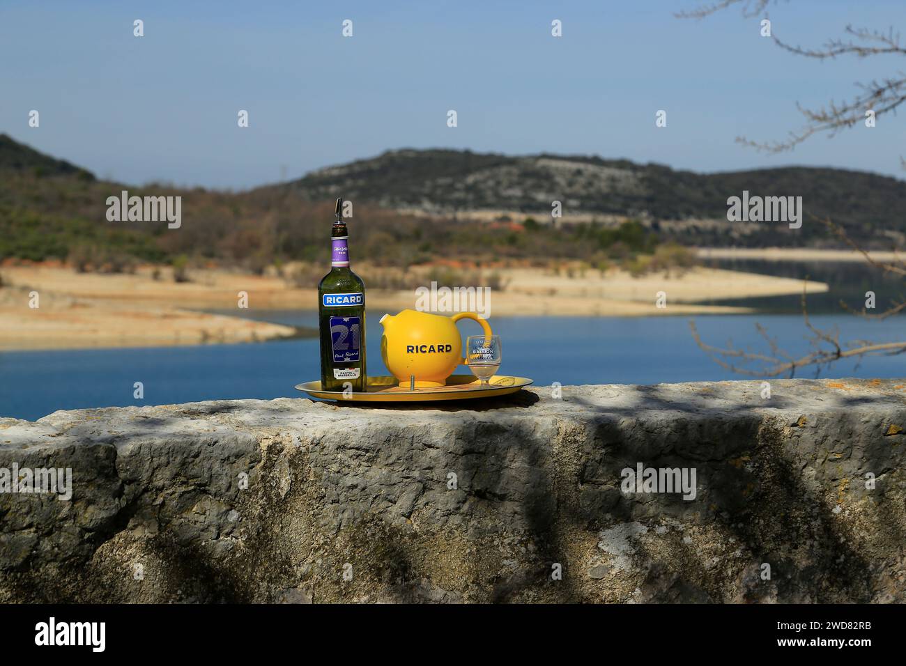 Ricard bottle, glass and jug, sitting on a wall, overlooking lake in Provence, France. Stock Photo