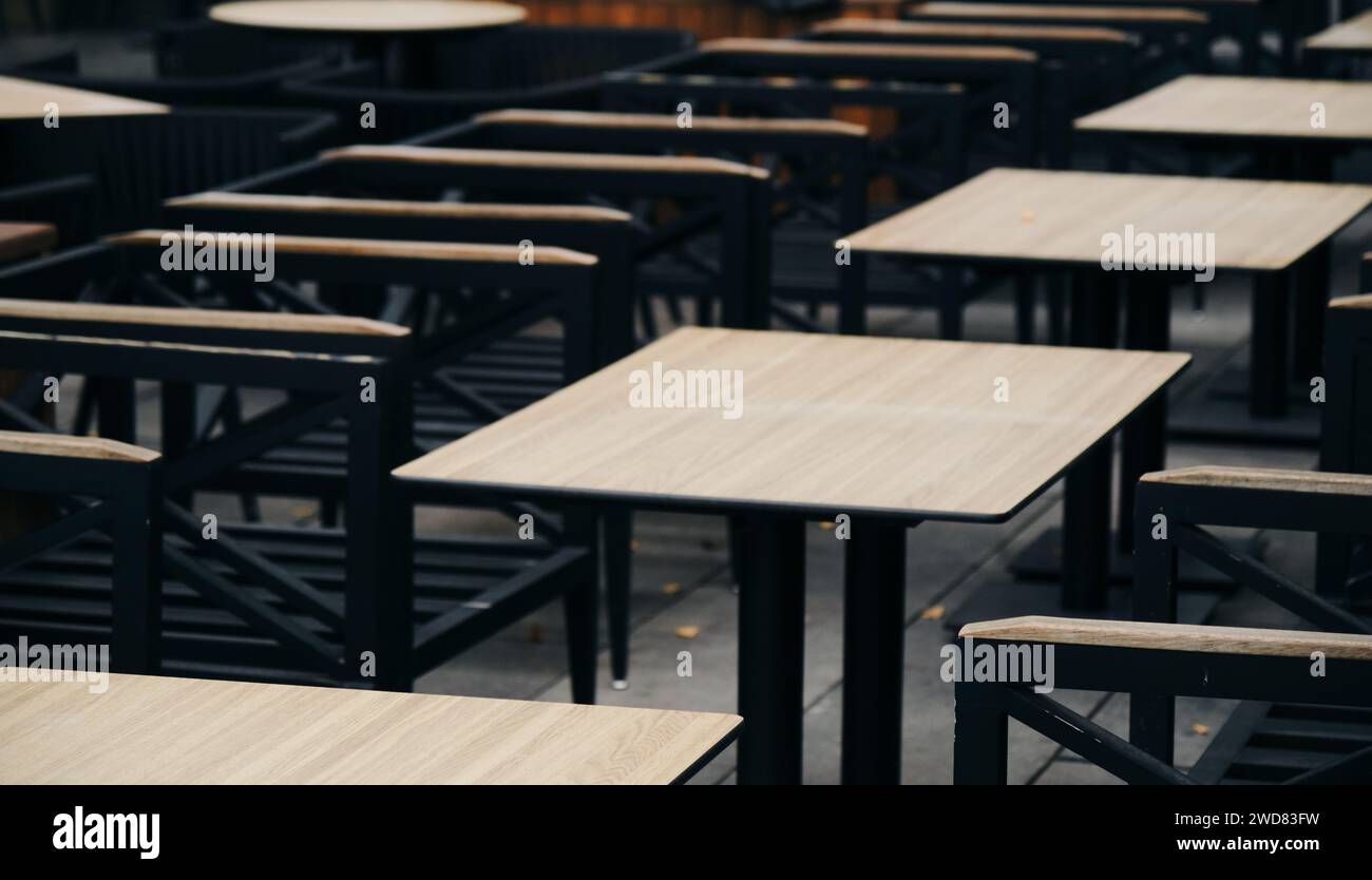 Empty wooden tables and chairs in the cafe on the veranda in low season. The restaurant is ready to receive guests. A minimalistic blurred background Stock Photo
