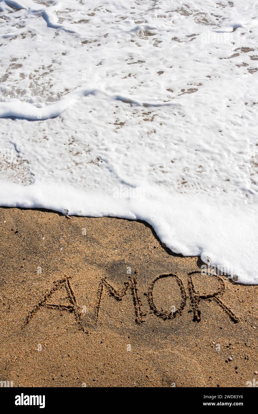 Love unveiled: 'Amor' etched in beach sands, embraced by a gentle wave, a poetic moment along the shore Stock Photo