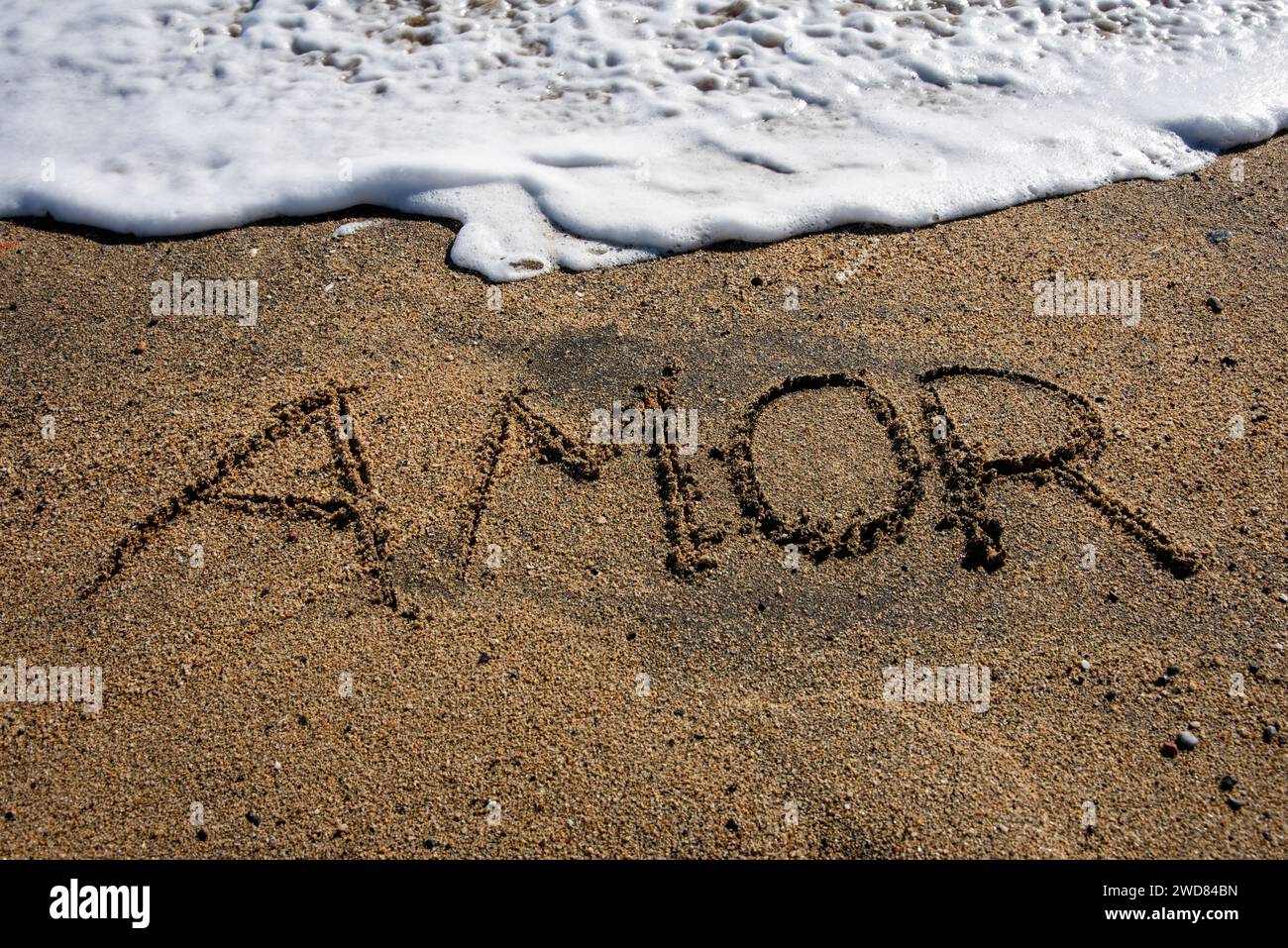 Love unveiled: 'Amor' etched in beach sands, embraced by a gentle wave, a poetic moment along the shore Stock Photo