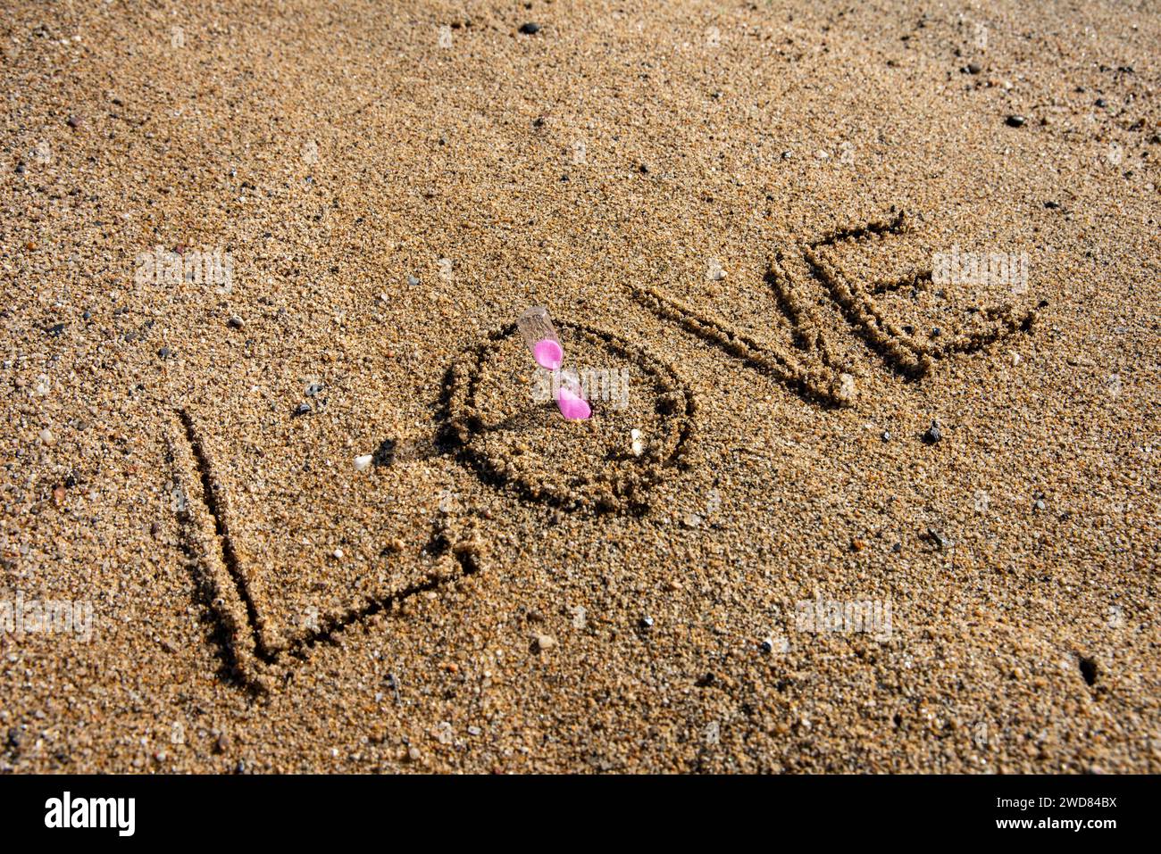 Timeless love: 'Love' inscribed on the beach, cradling a pink-hued hourglass, where romance meets the sands of eternal moments Stock Photo