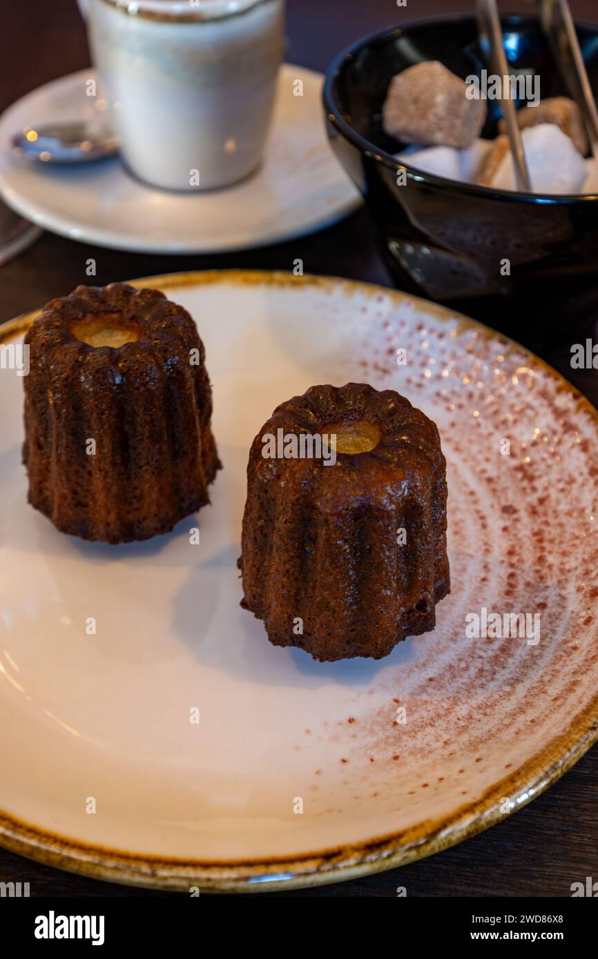 Canele, French pastry flavored with rum and vanilla, specialty of Bordeaux region, France, served on white plate with cup of black coffie in French re Stock Photo