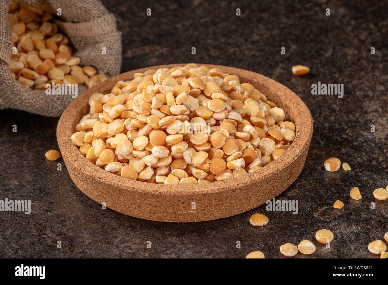 A rustic cork plate is displayed with a bountiful arrangement of fresh peas atop a dark background, illustrating a culinary concept and healthy cookin Stock Photo