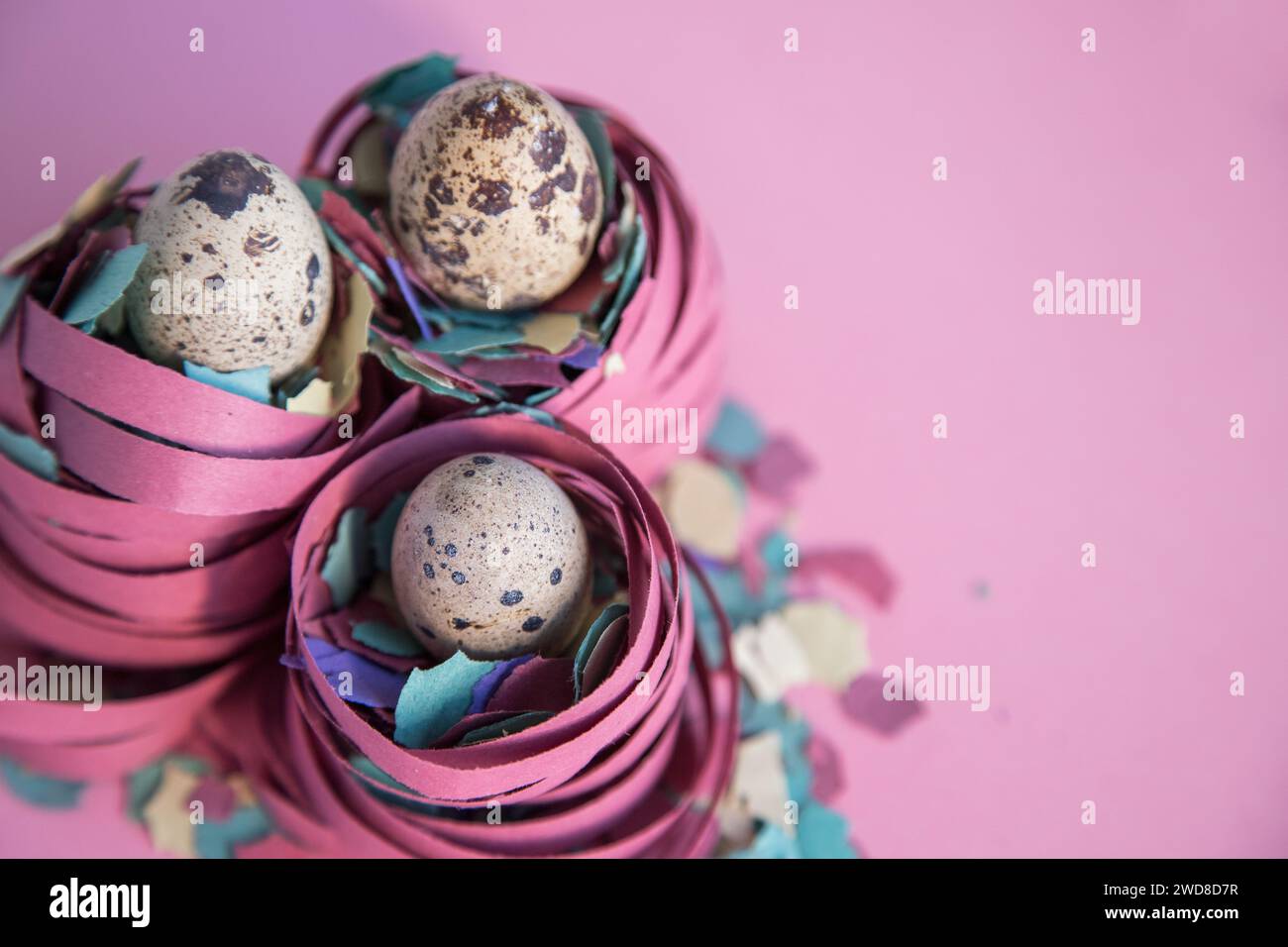 Close-up of three small quail eggs above a nest of confetti and streamers. Concept of fragility and protection, transition from Carnival to Easter. Stock Photo