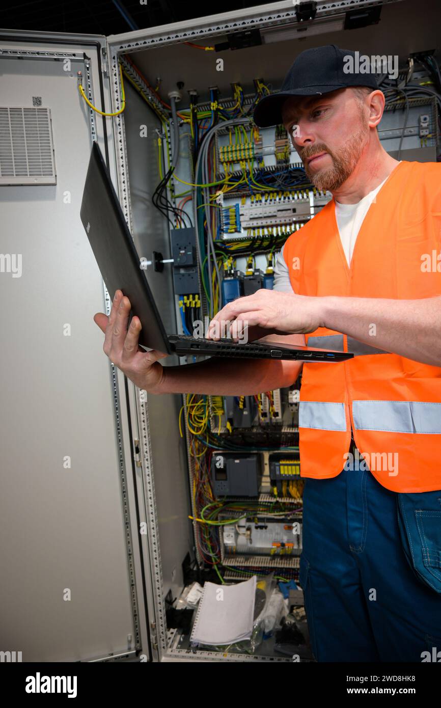an electrician in a cap and orange vest installs a large electrical ...