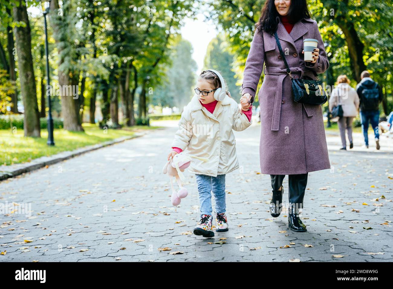 Disabled child is walking in the outdoor park like other people. Little girl has a young mom to take care of closely, Life in the education age of Stock Photo