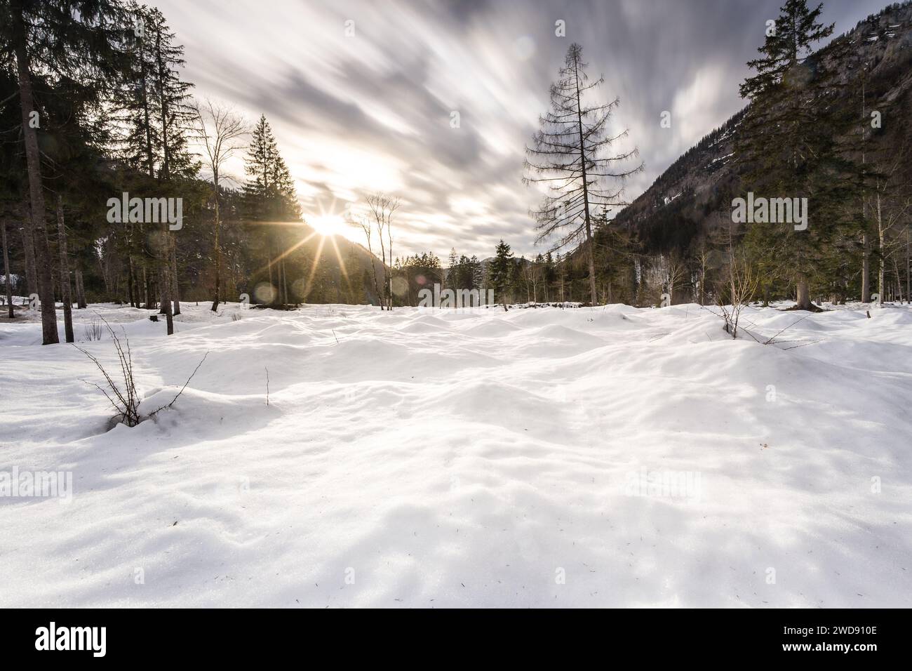 Sun shining through clouds behind snowy landscape Stock Photo