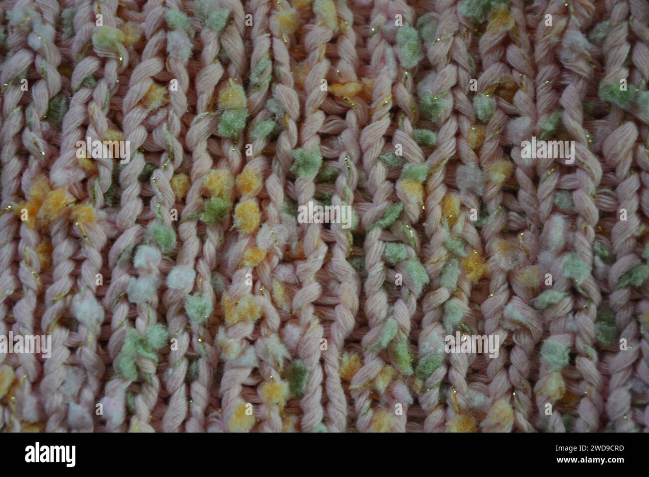 Hand weaving, knitting. A beautiful patterned background is knitted from pink threads with colored inserts. Stock Photo
