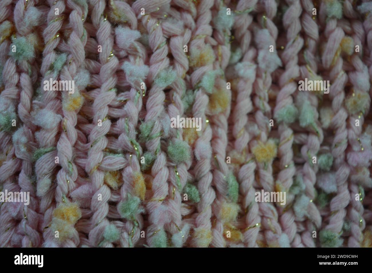 Hand weaving, knitting. A beautiful patterned background is knitted from pink threads with colored inserts. Stock Photo