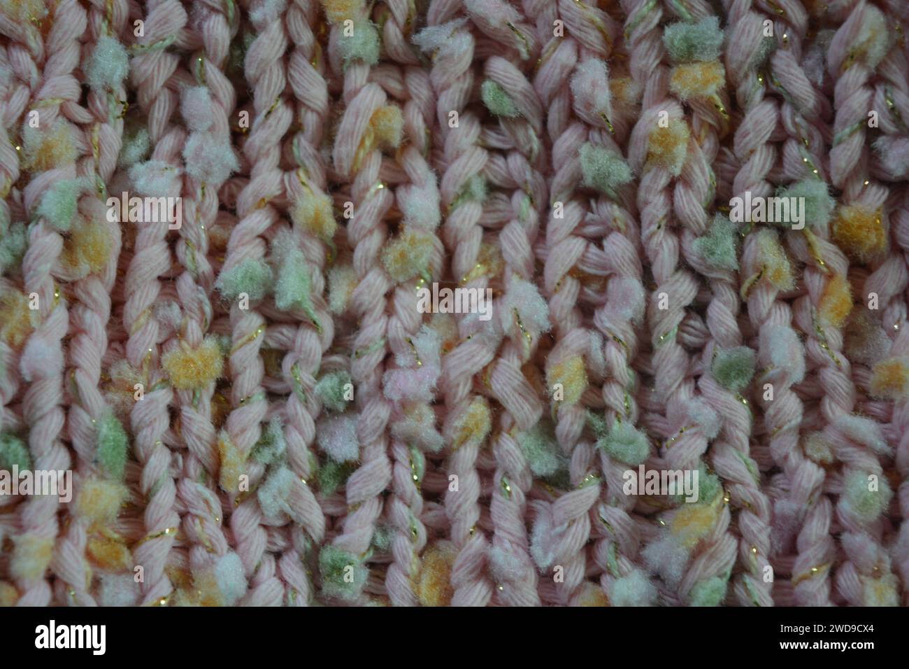 Hand weaving, knitting. A beautiful patterned background is knitted from pink threads with colored inserts. Stock Photo