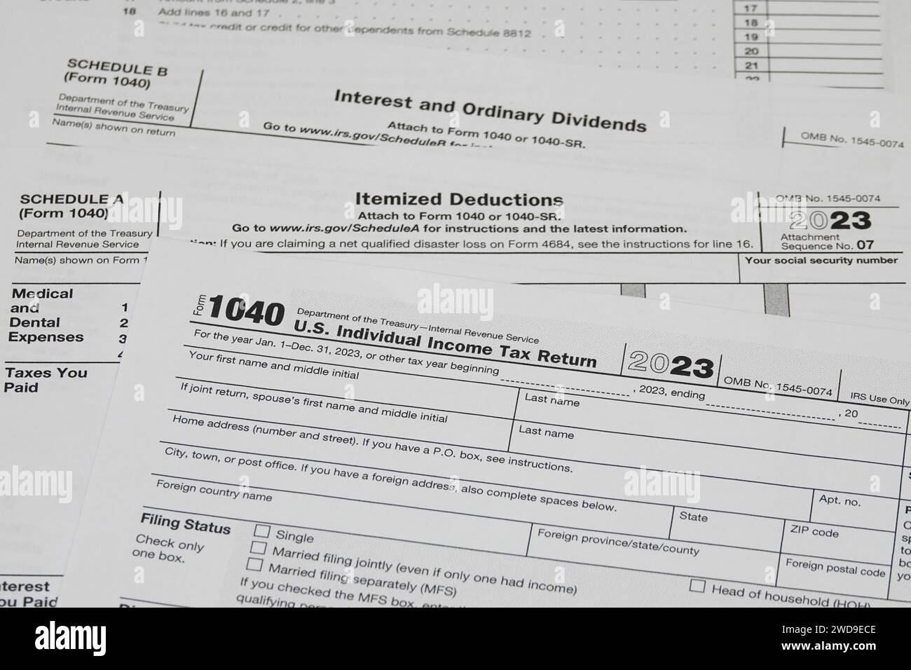 In 2024, for tax year 2023, a printed IRS 1040 tax form is shown, along with Schedule A and Schedule B forms. Stock Photo