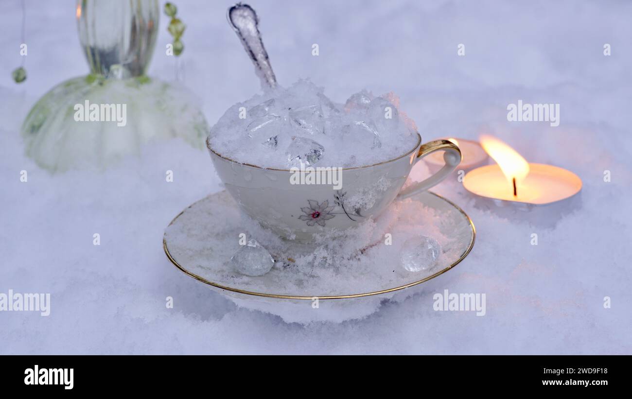 A cup filled with ice in the snow. Glass crystals. Lit tea lights. Table layed for the ice queen. Stock Photo