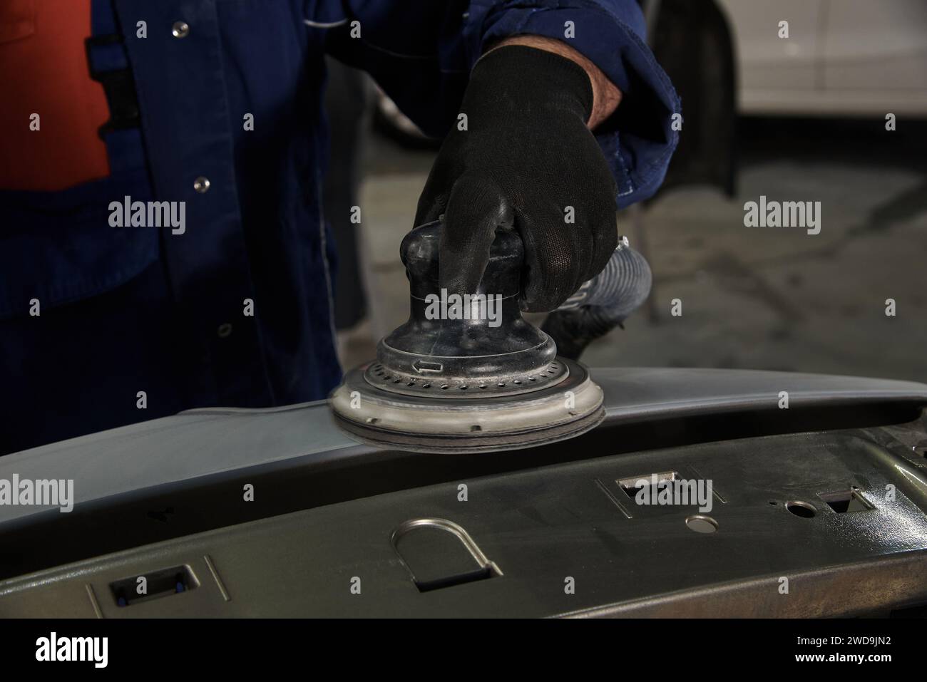 A man at a car maintenance station cleans the car part with an instrument. Preparation of car parts for painting. Car repair at the station. Car servi Stock Photo