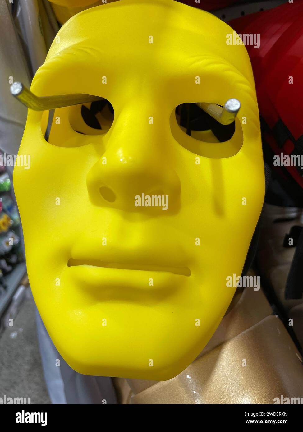 A bright yellow plastic mask on display, with metallic pins put into ...