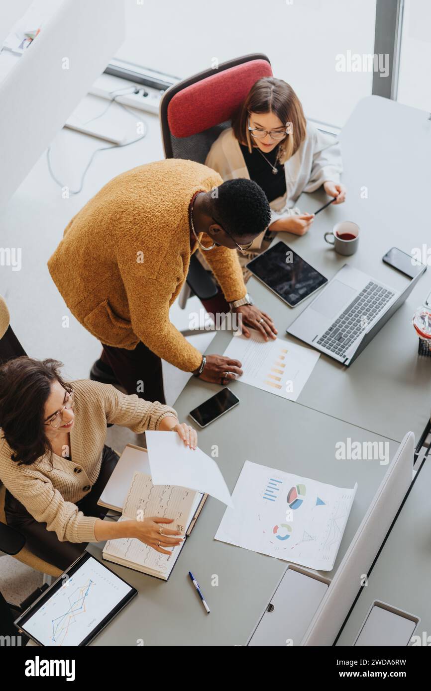 Diverse team collaborating on project with digital devices and paperwork. Stock Photo