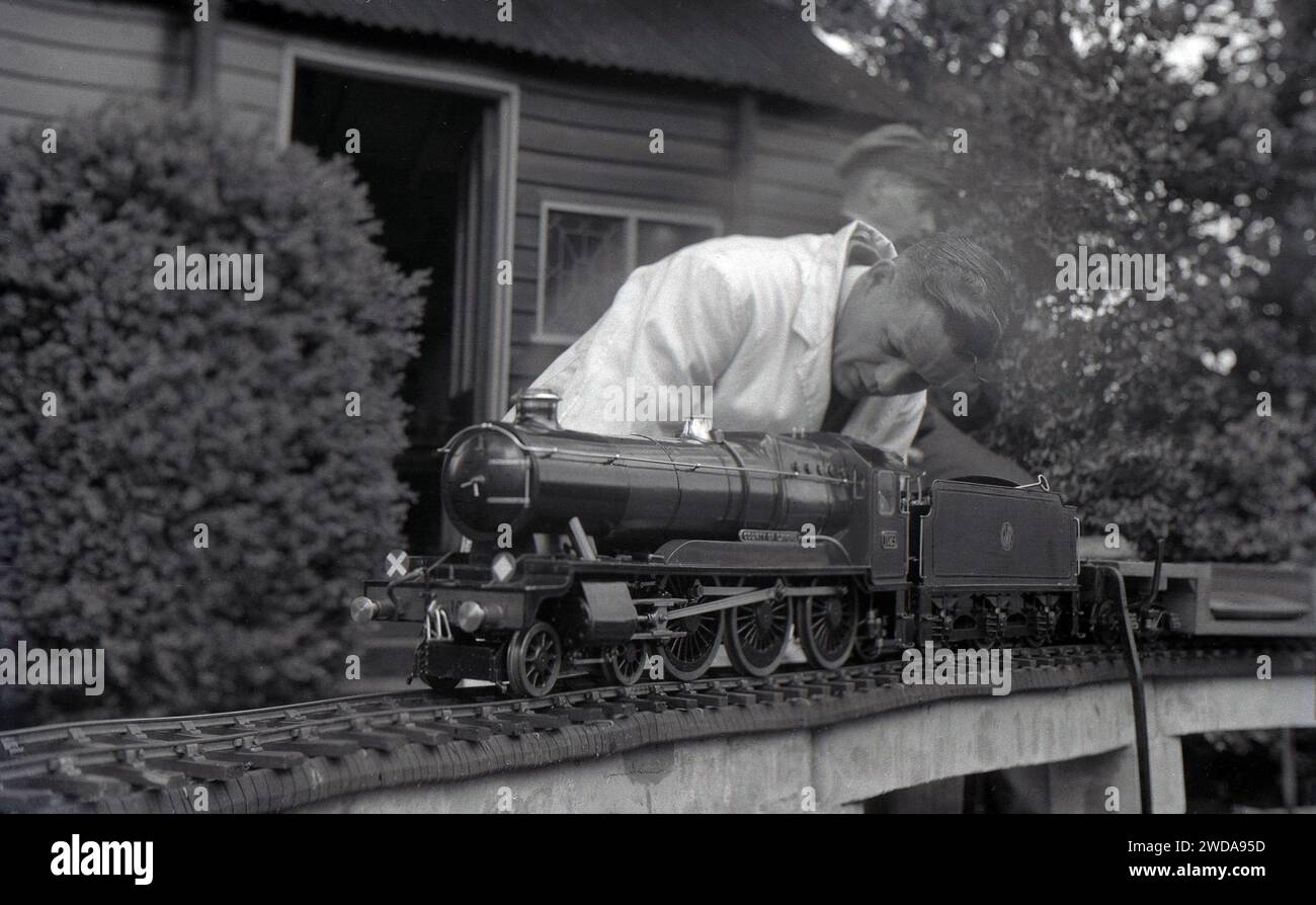 1950s, historical, outside in the garden of the Field End Railway Co, England, UK, a model steam railway enthusiast in a white-coat working on a miniature steam train, 'County of Oxford', a GWR steam locomotive which entered service in 1947. Stock Photo