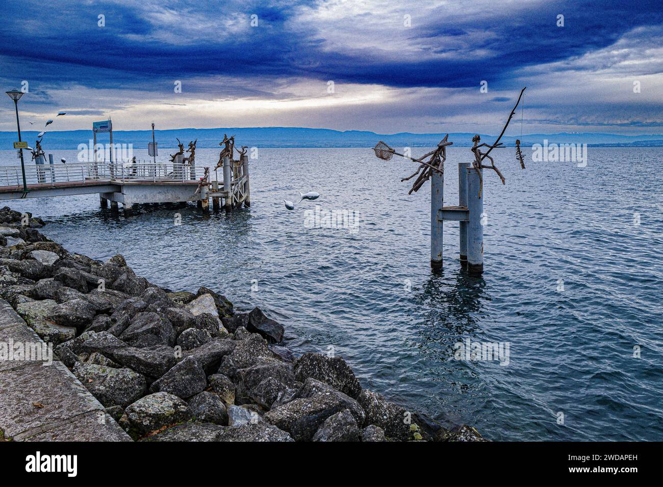 Several metallic birds perched on poles in the water along a pier Stock Photo