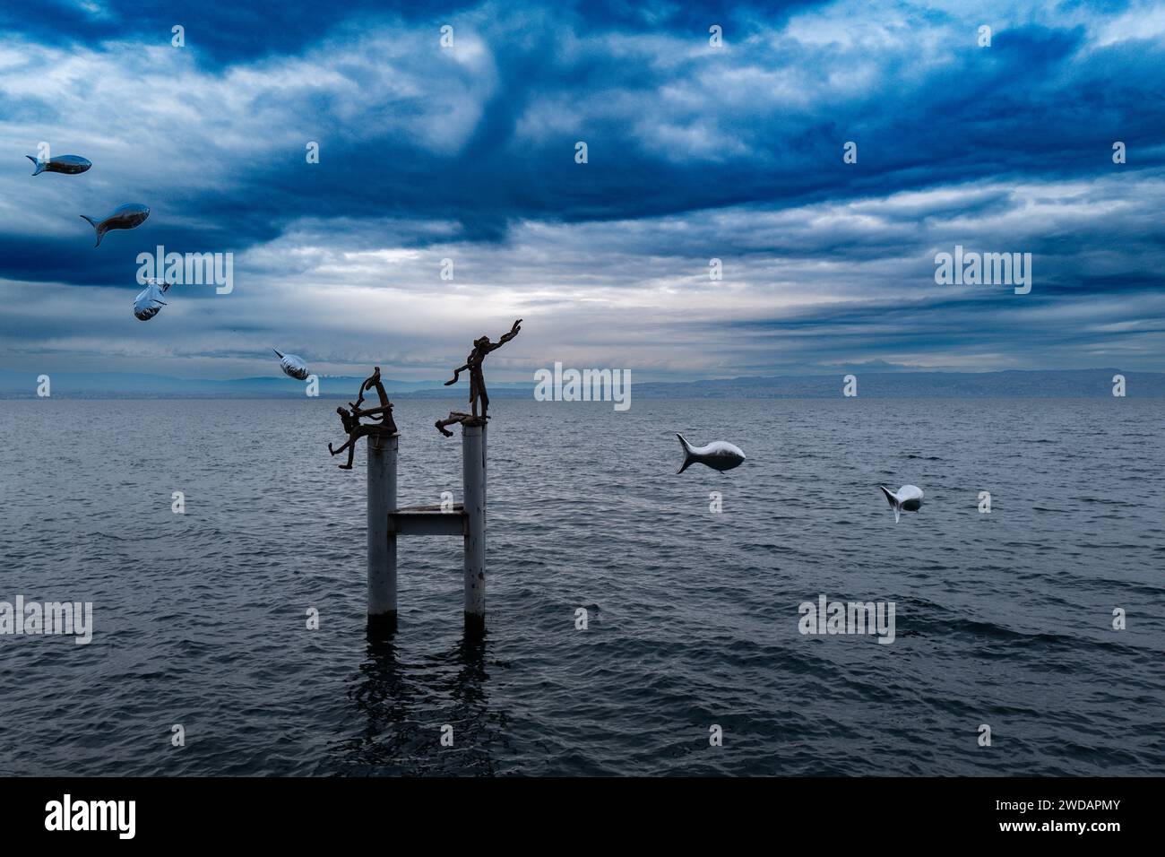 Two individuals perched atop a pole amidst the vast ocean Stock Photo