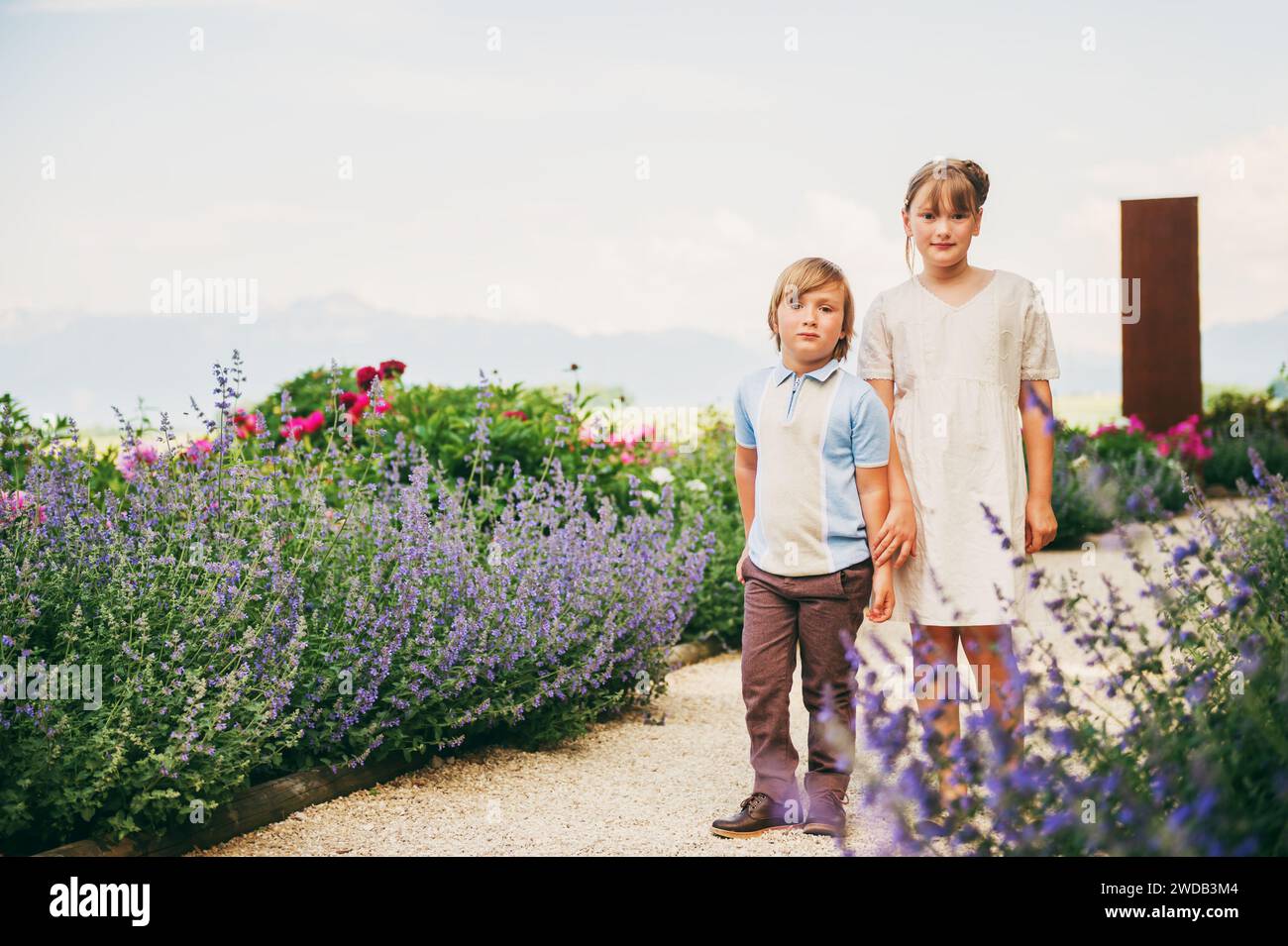 Fashion kids posing in beautiful garden, wearing vintage style clothing. Summer blooming lavender and peonies Stock Photo
