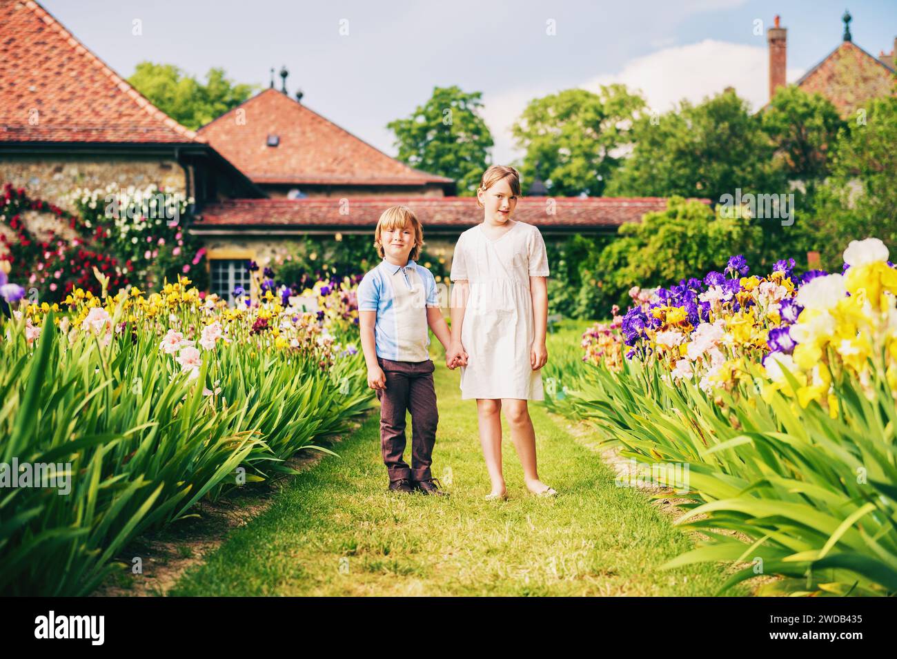 Group of two kids, little boy and girl, posing in beautiful english style garden, wearing retro style clothing, holding hands. Brother and sister play Stock Photo