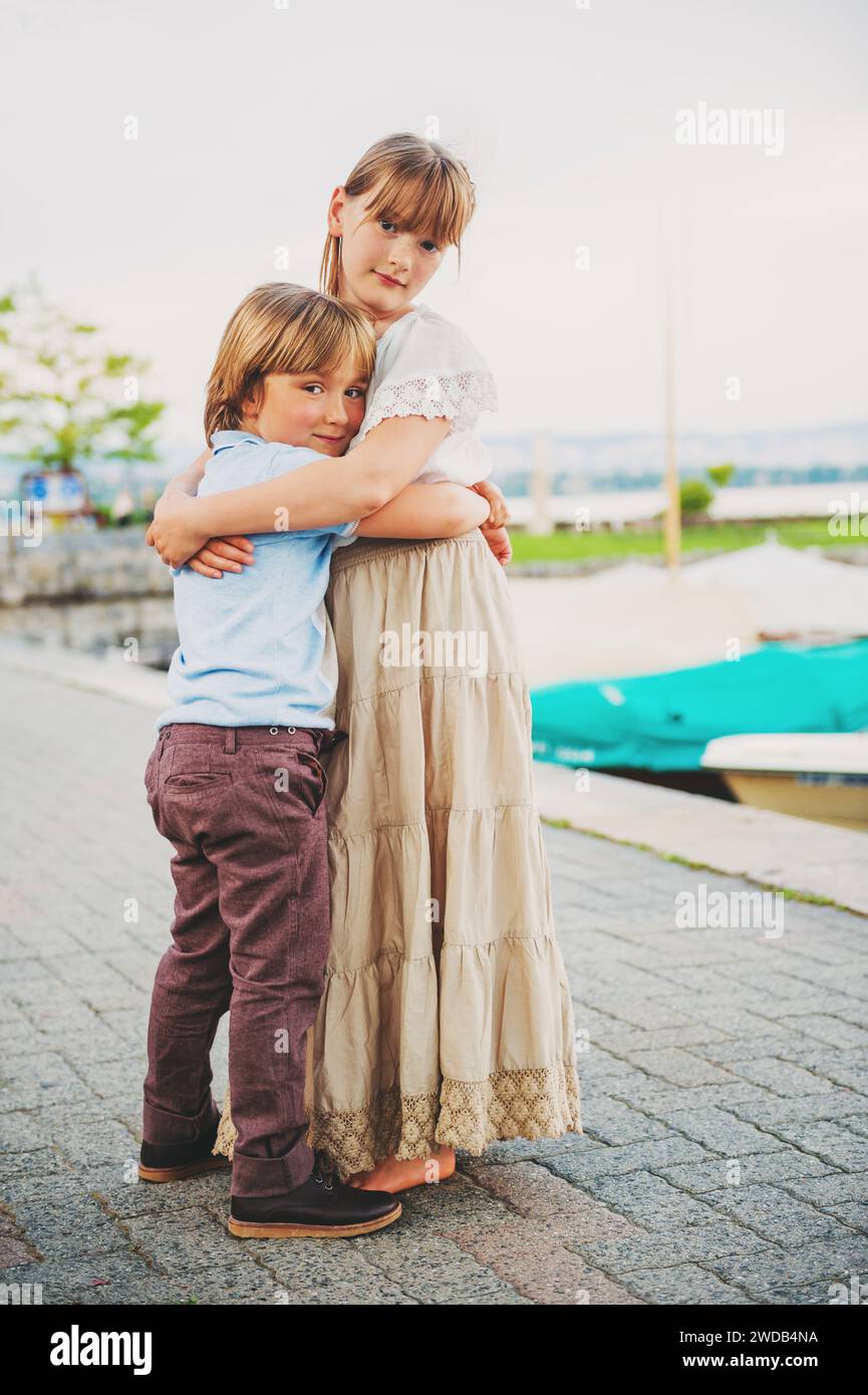 Outdoor portrait of two adorable kids hugging each other, little boy and girl spending time together, vertical image Stock Photo