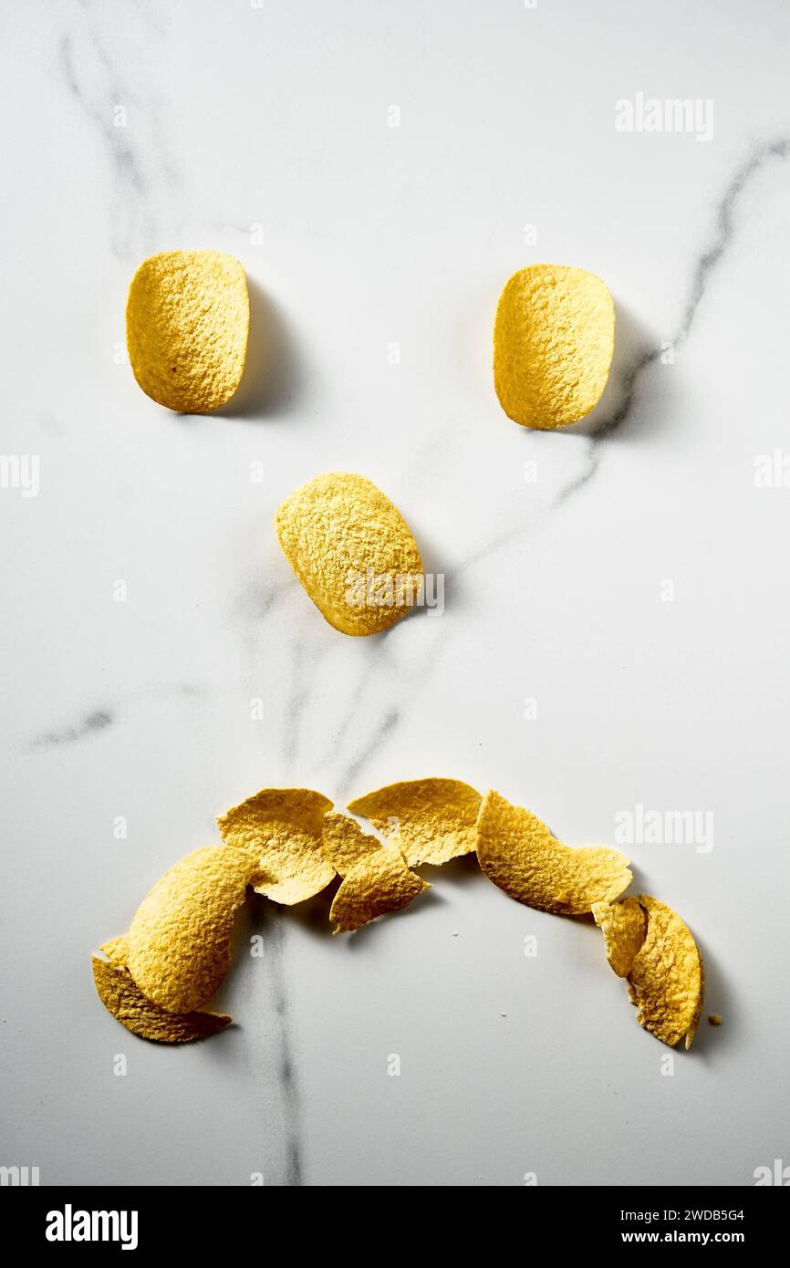 Potato chips shaped like a sad smiley face on white marble background