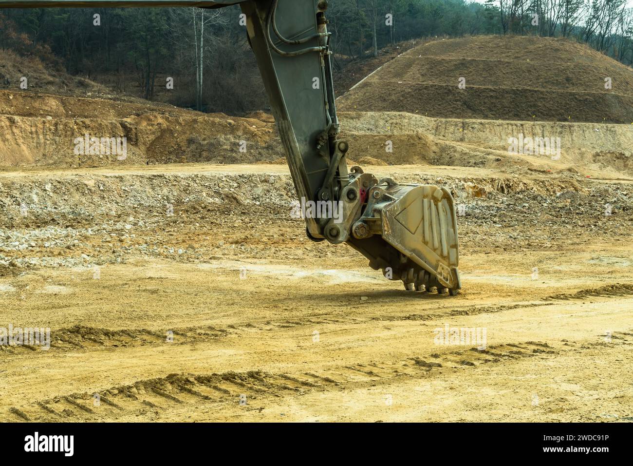 Backhoe hydraulic arm with attached bucket resting on ground at