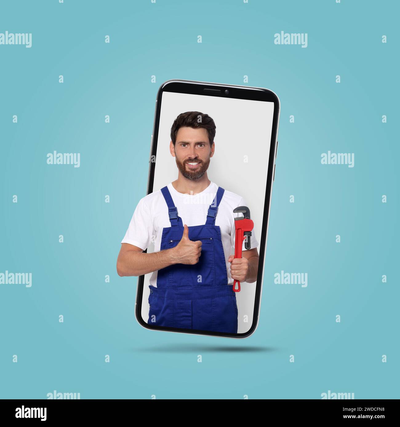 Plumber looking out of smartphone and showing thumbs up on light blue ...