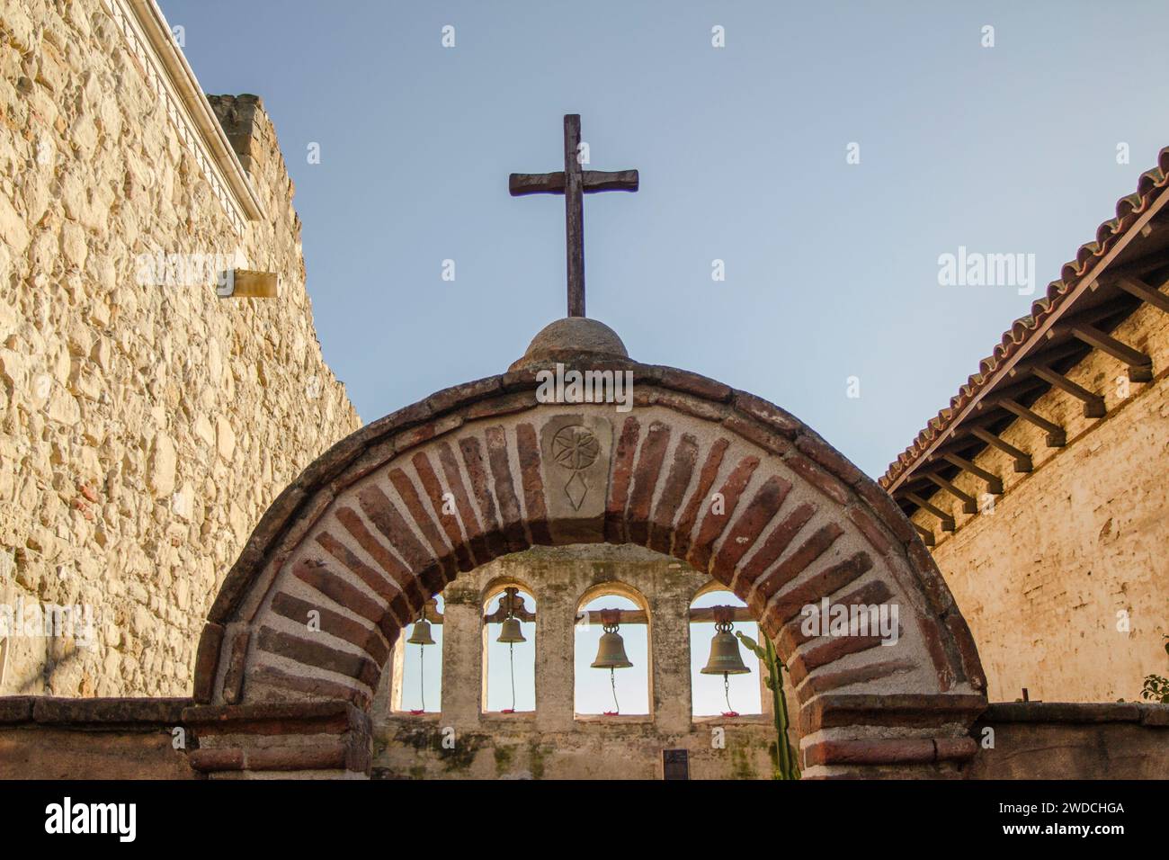 Wooden cross on top of an arch with bells at Mission San Juan ...