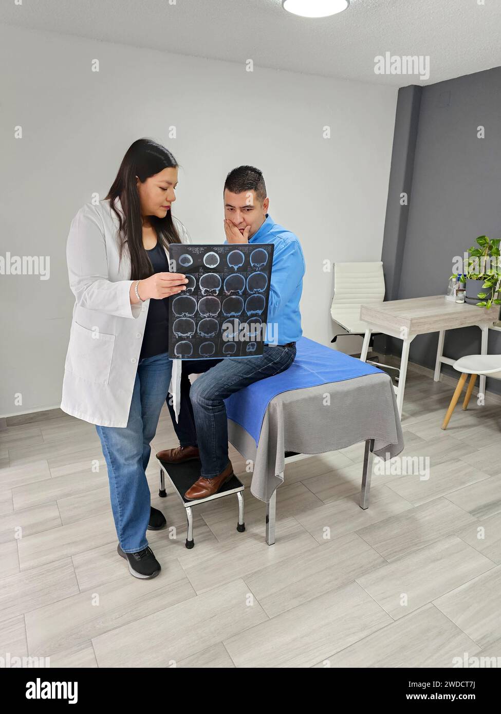 Female doctor, Latina neurologist, attends to male, brunette patient in her office, shows brain x-ray to evaluate head injuries and brain disorders Stock Photo