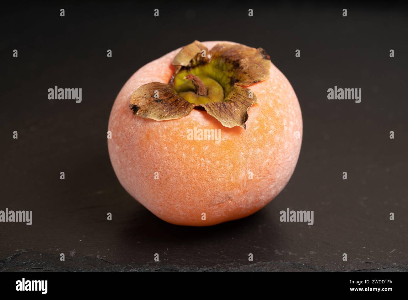 Frozen food. Frozen persimmon covered with frost melting on a black ...