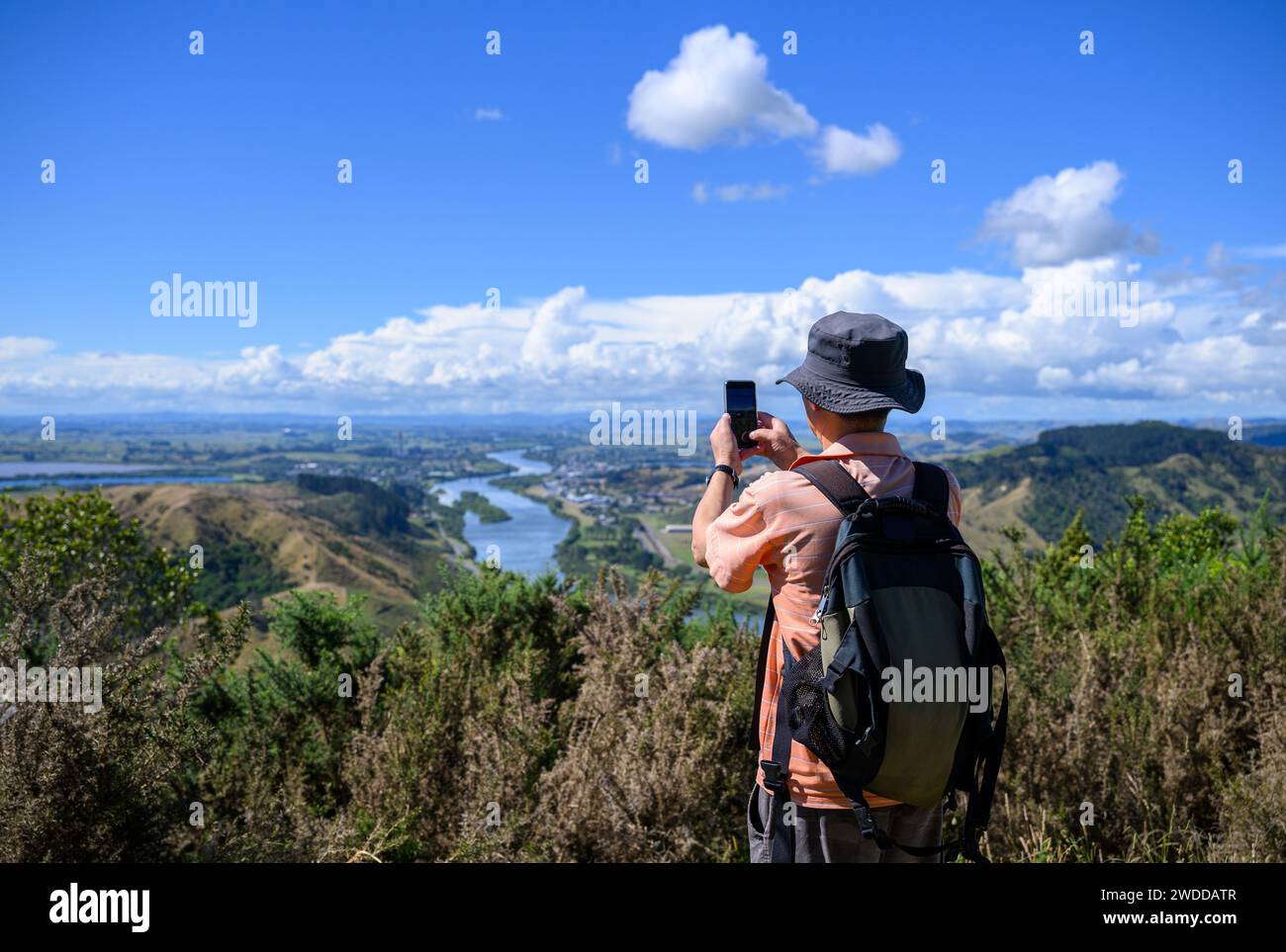 Man taking photos using smartphone of Huntly and the north Waikato lakes. Hakarimata Summit Track. Huntly. New Zealand. Stock Photo