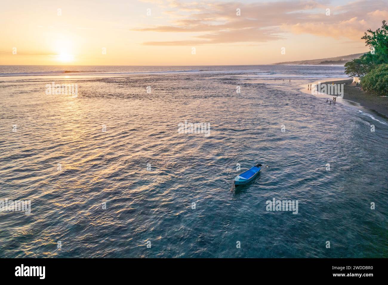 An elegant aerial view of a boat on a beach, during a magnificent sunset. Tourists swimming and enjoying the view. Étang-Salé, Reunion Island. Stock Photo
