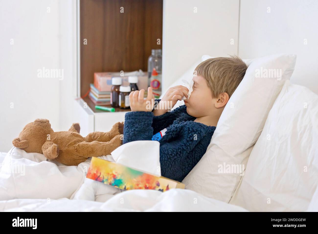 Sick child, toddler boy lying in bed with a fever, resting at home with