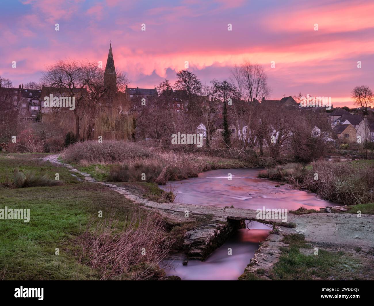 Saturday, January 20th 2024. Malmesbury, Wiltshire, England - As the sun rises across the frozen watermeadow and ancient clapper bridge, the sky turns red above the picturesque Wiltshire market town of Malmesbury. Credit: Terry Mathews/Alamy Live News Stock Photo