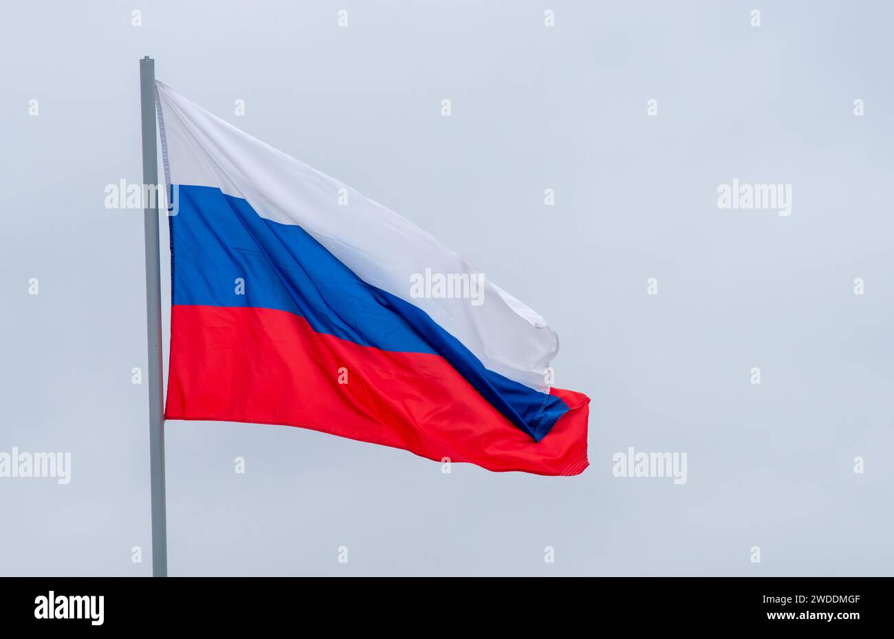 The white-blue-red flag of the Russian Federation is flying in the wind against a cloudy sky. Stock Photo