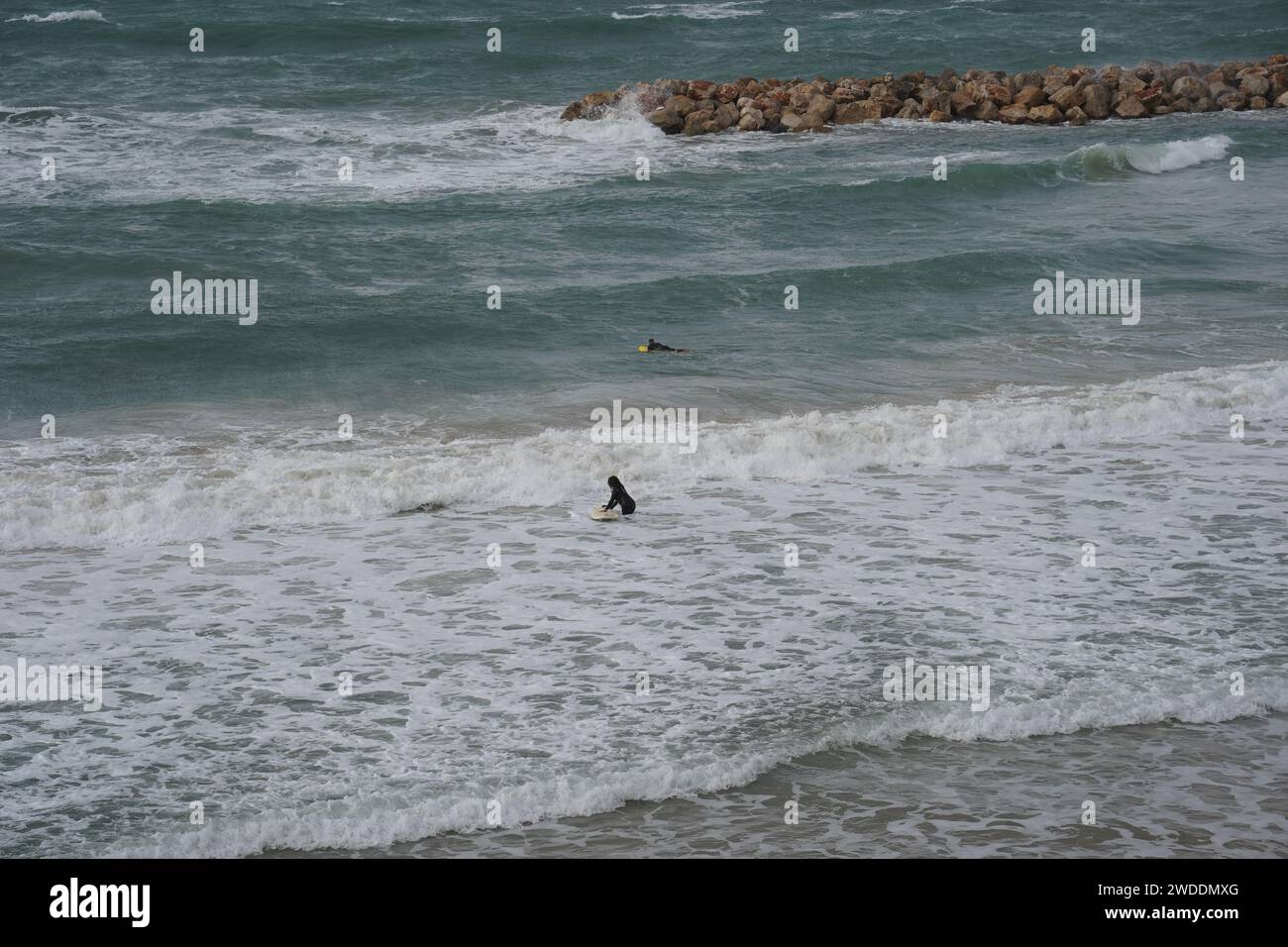 Strong currents and waves in the sea and surfers. Waves successfully crash into the stone breakwater. Stock Photo
