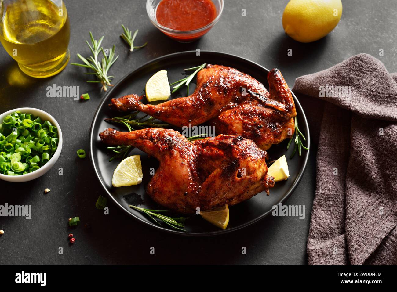 Grilled half chicken with lemon and rosemary on black plate over dark stone background. Tasty roasted chicken meat for dinner. Close up view Stock Photo